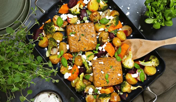 Örtmarinerad tofu ugnsrostade grönsaker på en svart plåt, till artikeln nyttig vegetarisk mat