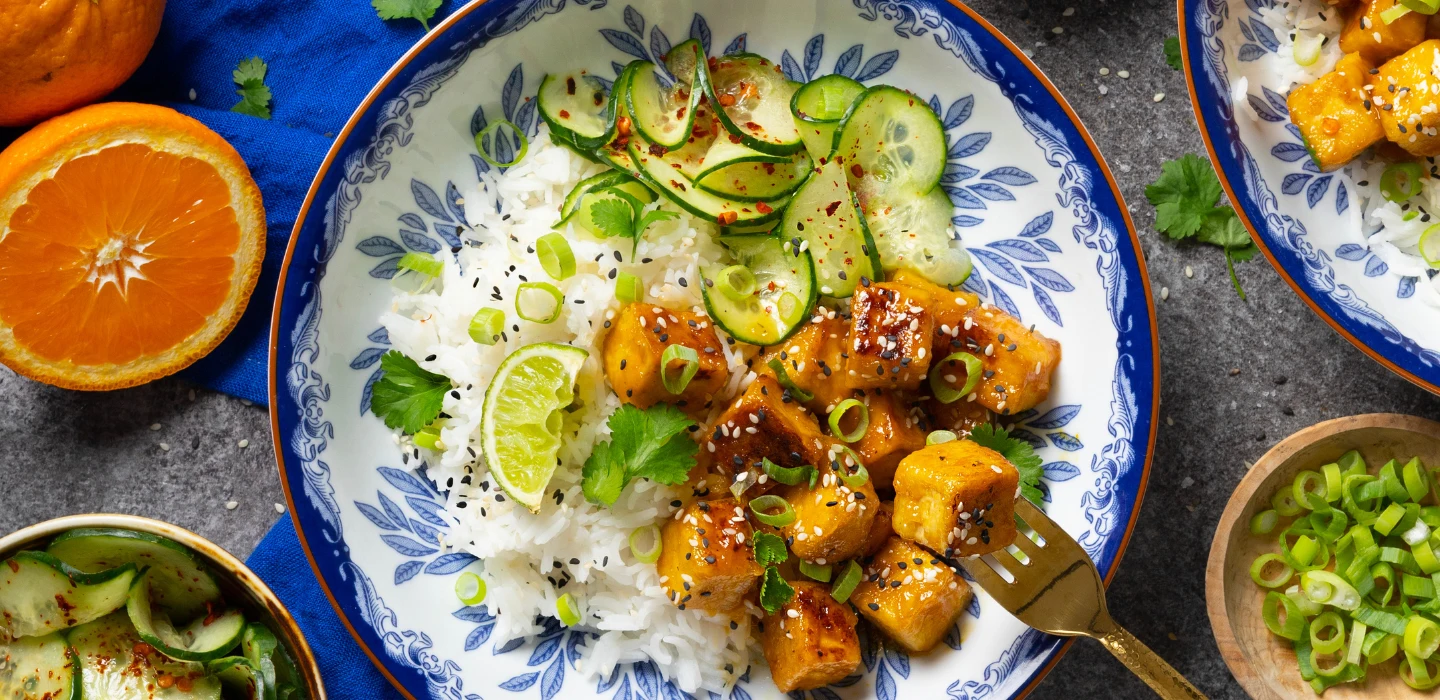 Bilden visar en tallrik med orange tofu, ris och chiligurka.